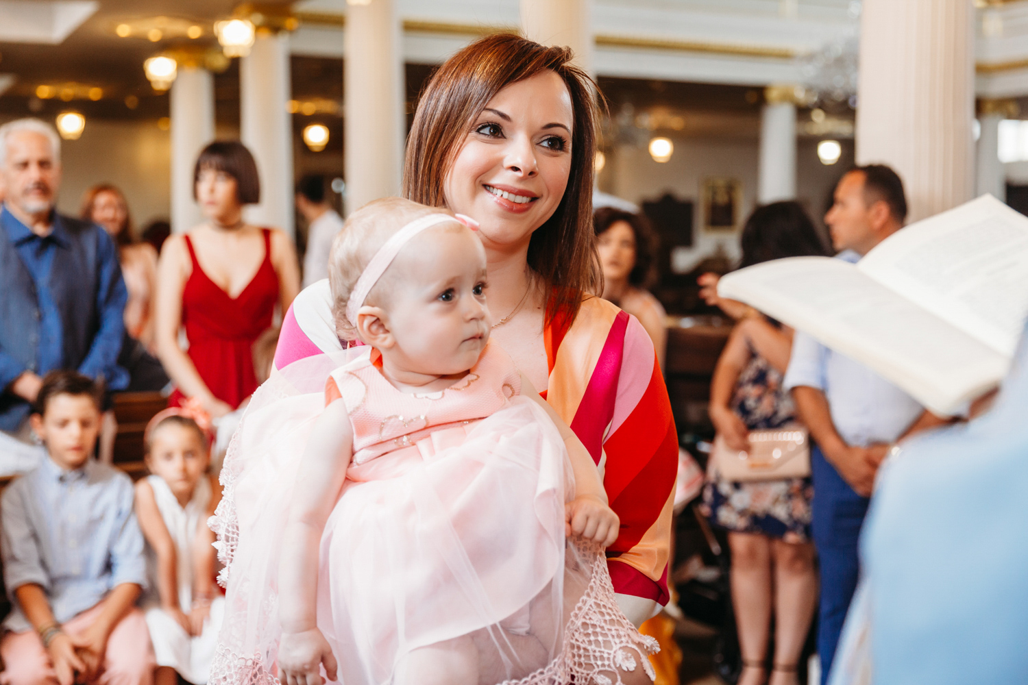 A godmother holding a little girl during her christening blessings reading.