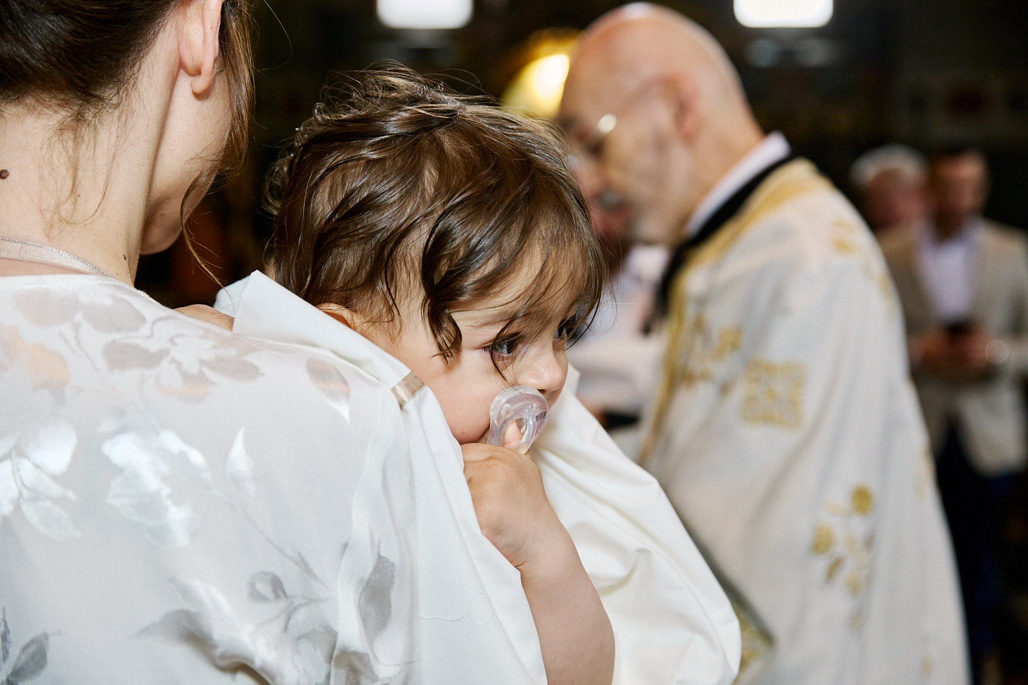 Little boy with his dummy, in his mum's arms, about to be christened.