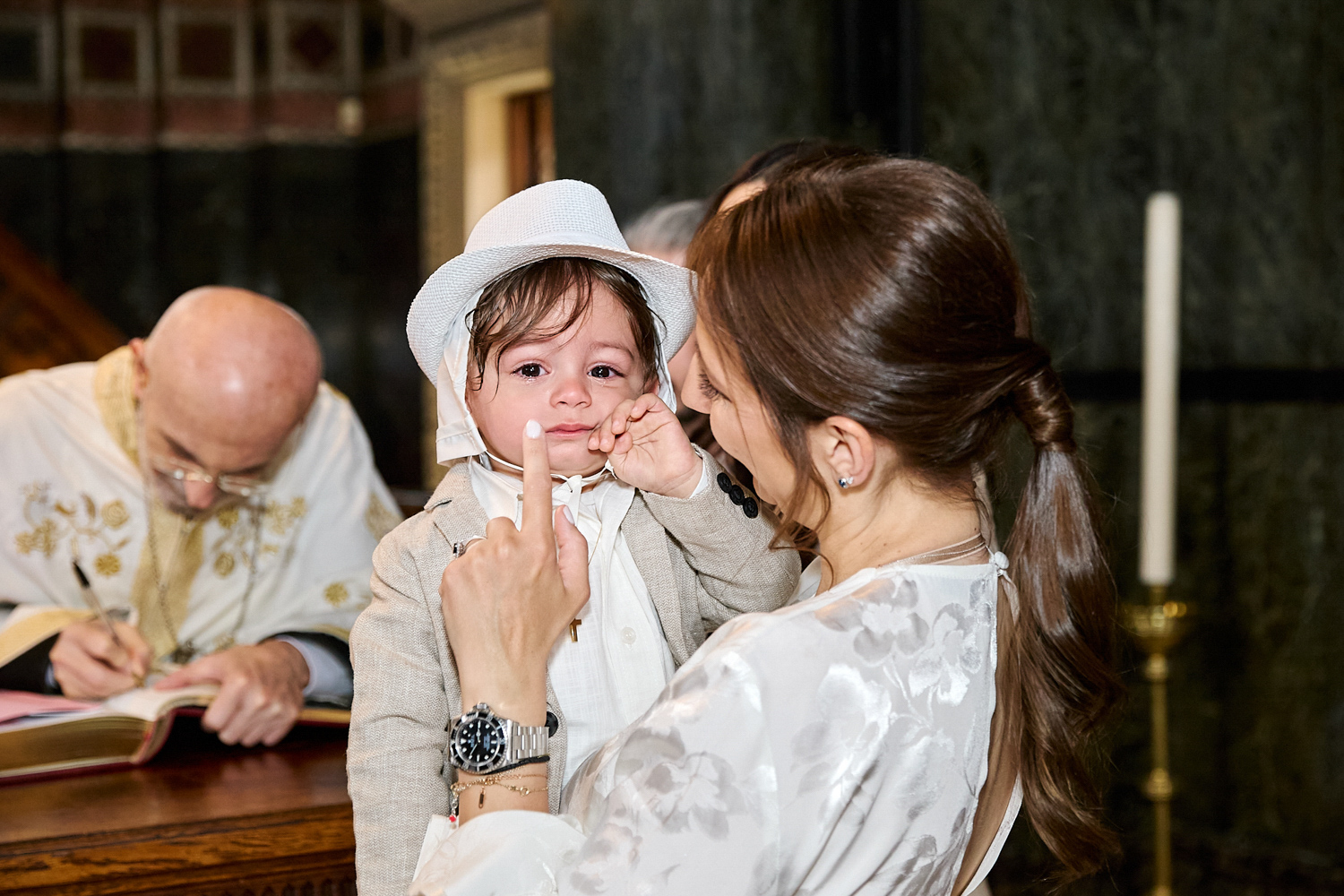 Little boy seems upset after being christened. He is held by his mum who's trying to comfort him.