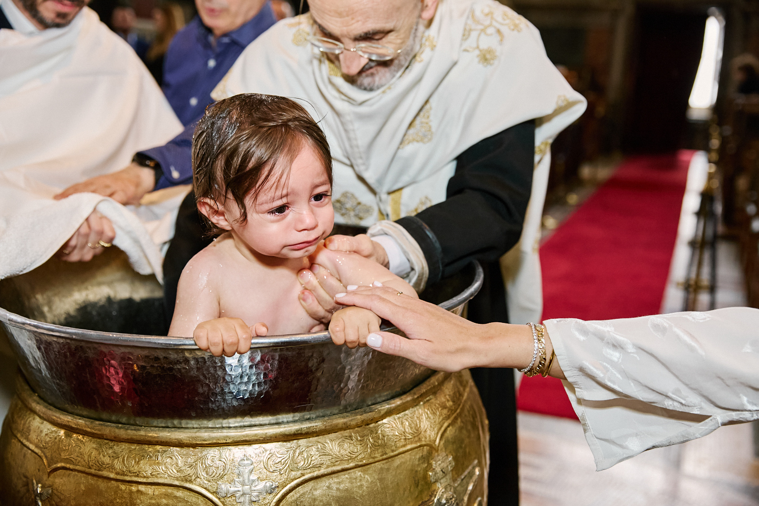 Mum holding his baby's hand and he is being christened.