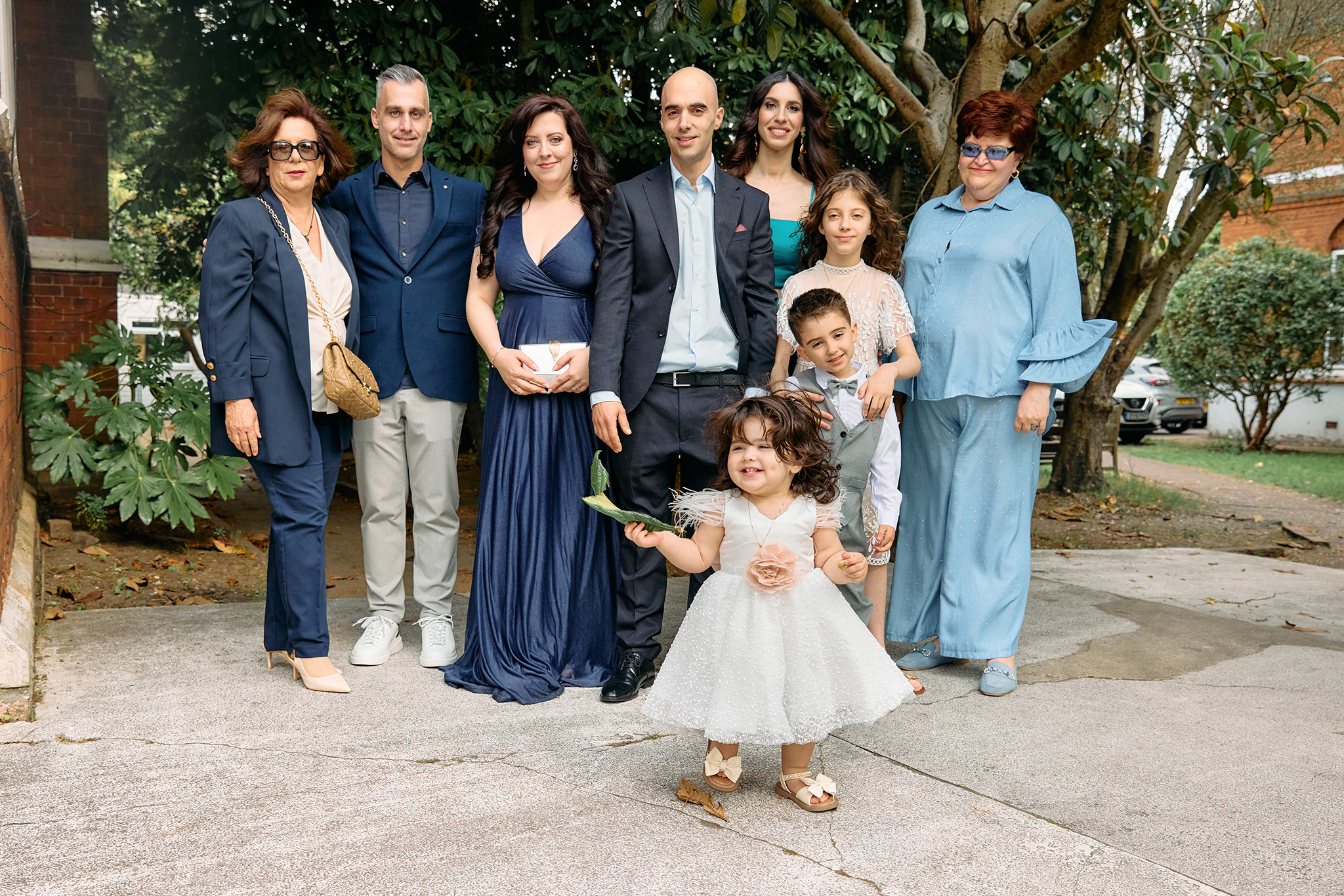 Family posig todether outside a church after their baby's christening. Little toddler standing happy in front of everyone.