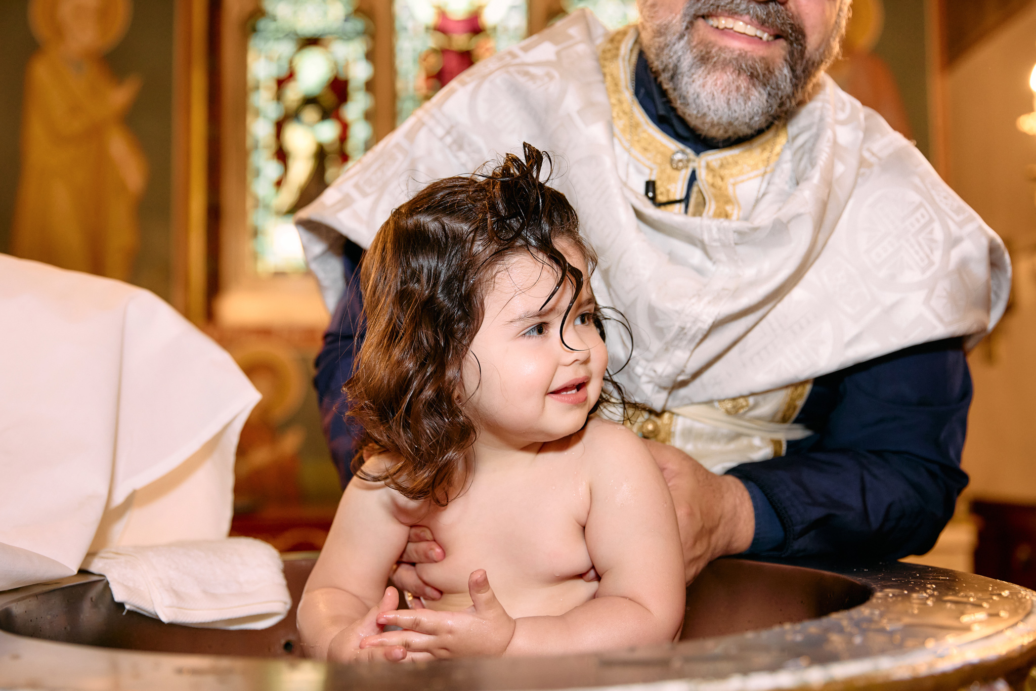 A little toddler being happy and smiling while being christened.