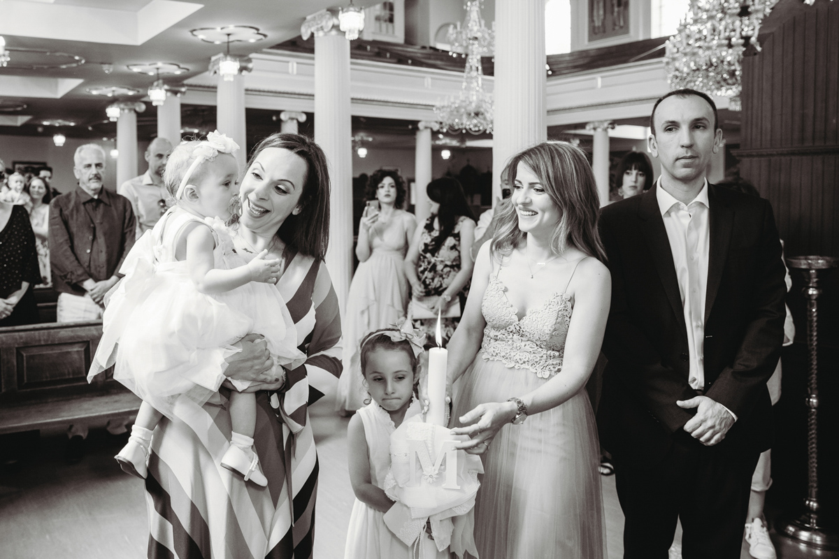 A documentary style photo of a godmother holding a baby and smiling during a christening.
