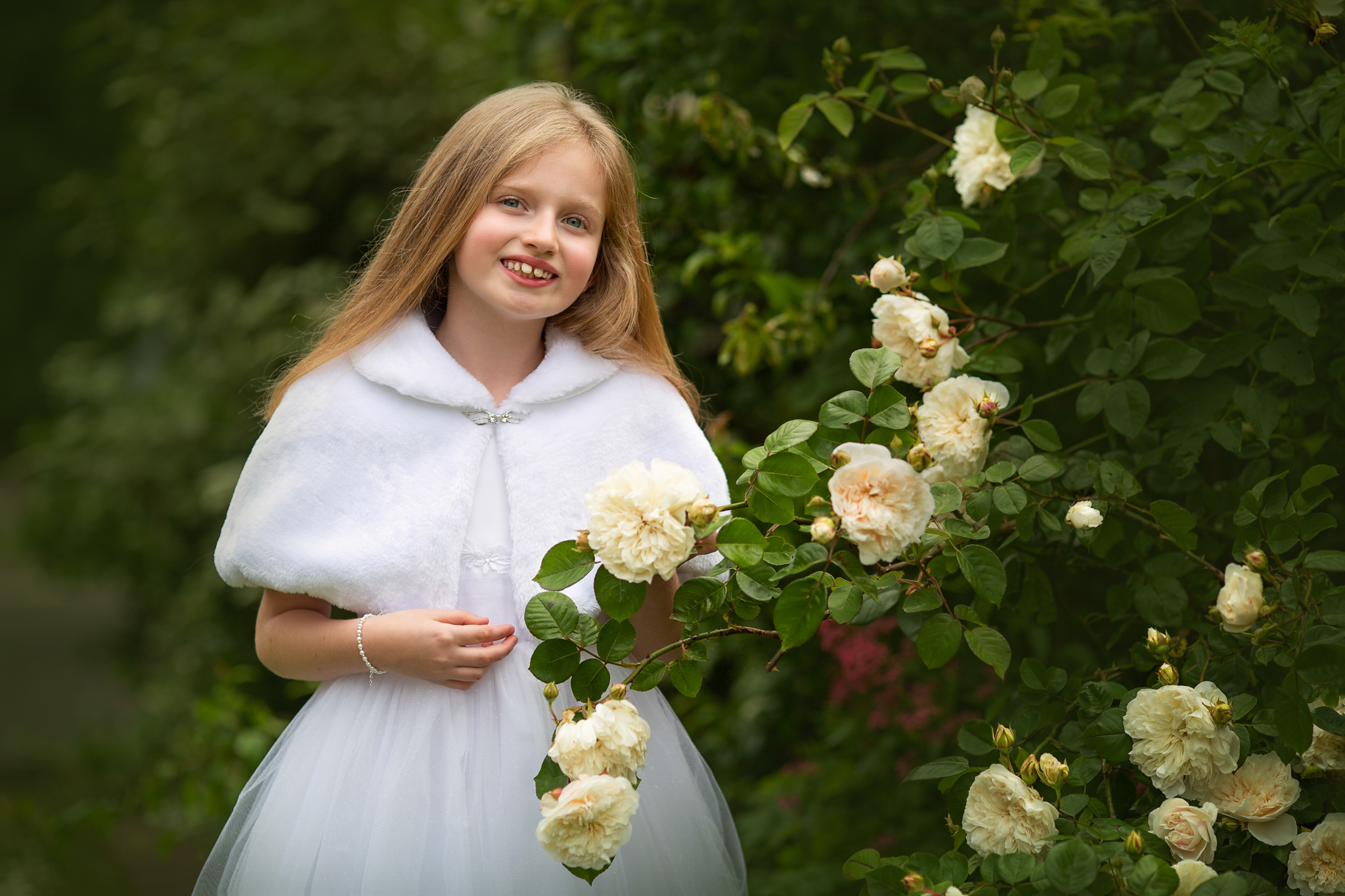girl in her white dress posing next flowers after her first communion in London