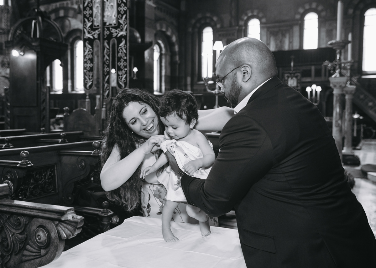 mum and dad dressing their newly christened girl in a London's Greek Orthodox church