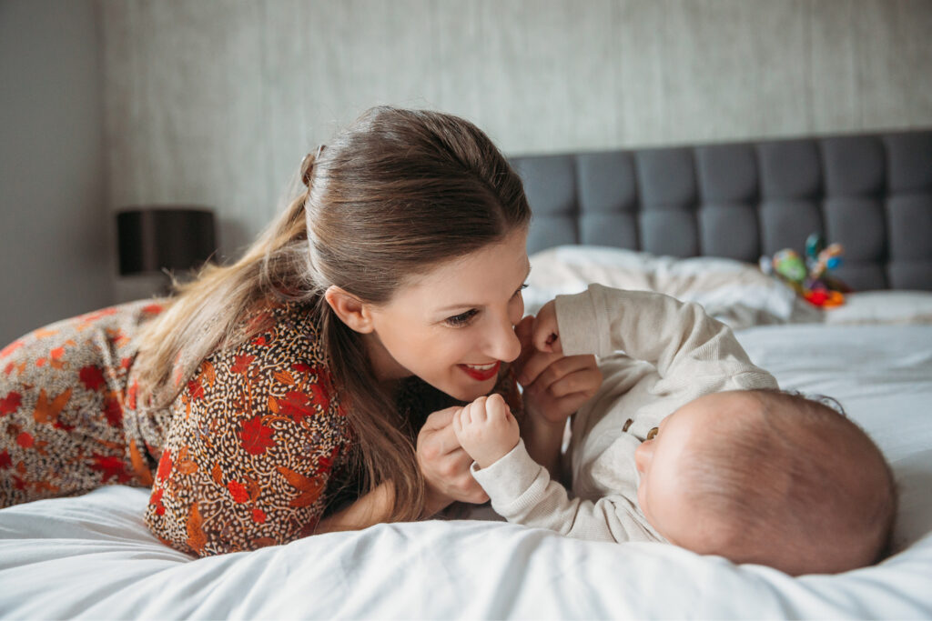 Mum is plalying with her baby in bed at their home.
