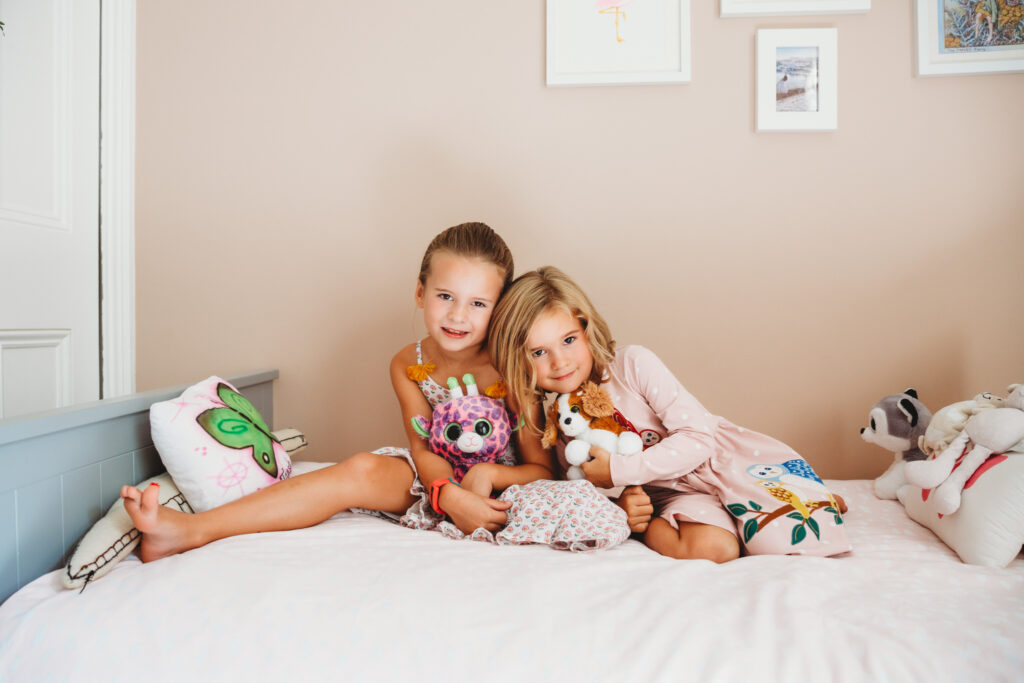 Two girl sisters sitting in bed next to each other smiling for a photo.