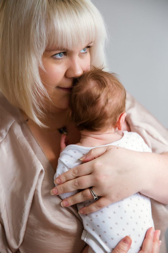 Mum holding her newborn baby looking out the wihdow feeling calm and happyl