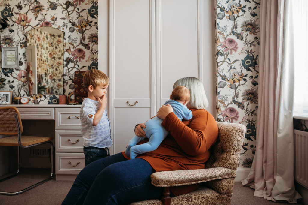 Little boy looking at his mum holding his newborn brother in a vintage decorated home in London.