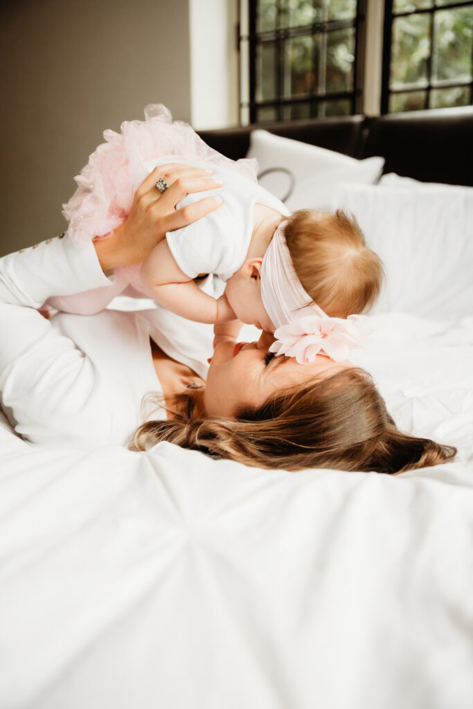 mum holding her baby up and bringing her close to her face while lying in bed.