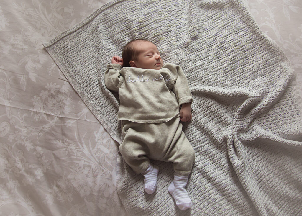 Newborn baby sleeping on his tummy in his light brown pyjamas.