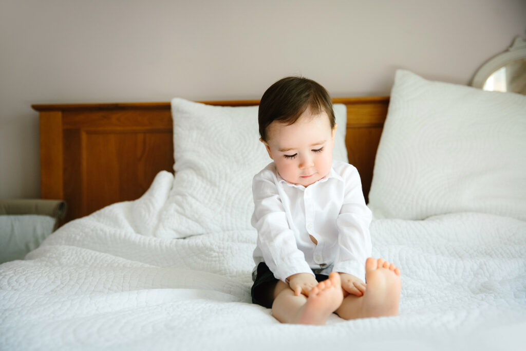Toddle sitting on bed with straight legs touching his knees.