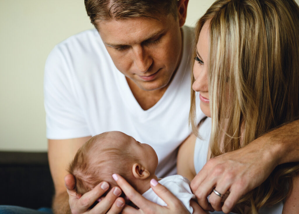 Dad hugging mum while they are both holding their newborn baby.