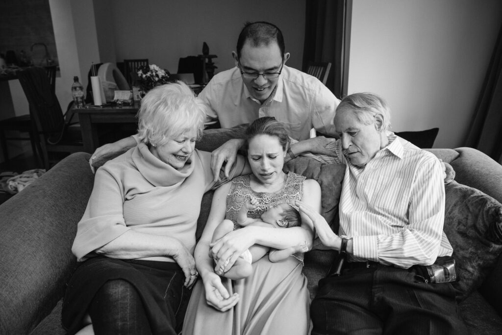 Domumentary style, black and white photo of a crying baby while everyone, including granma, granpa, mum and dad are trying to calm him down.
