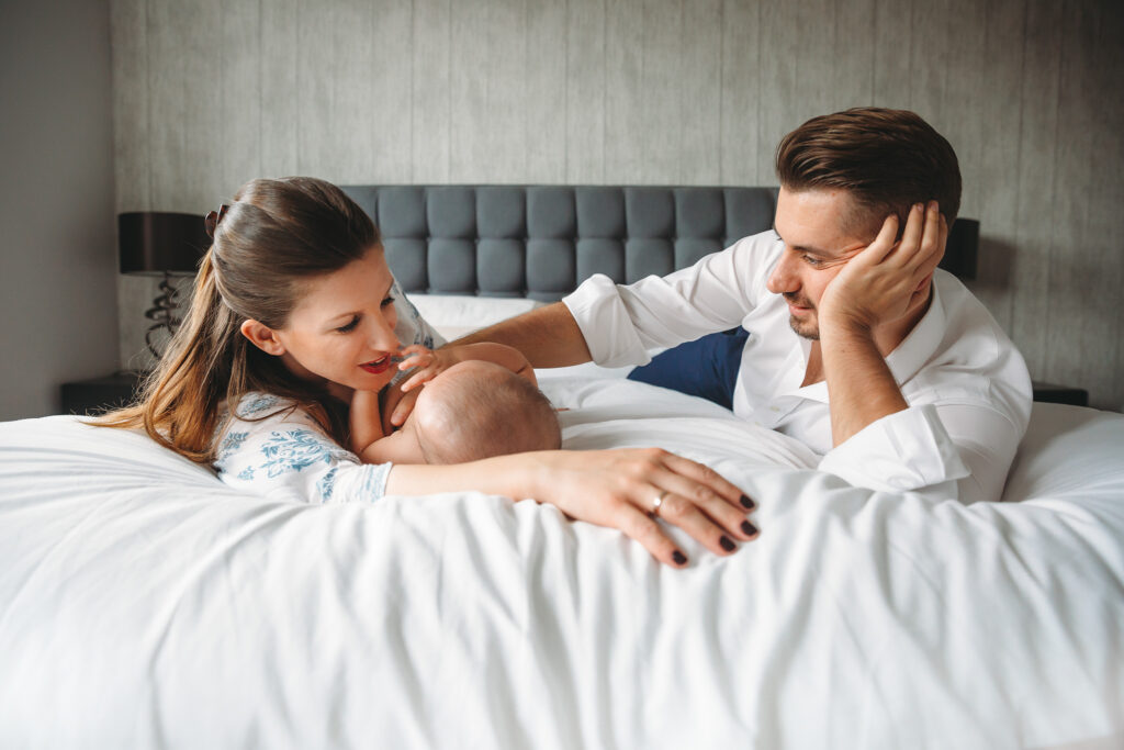 Mum and dad playing with their newborn baby in bed.