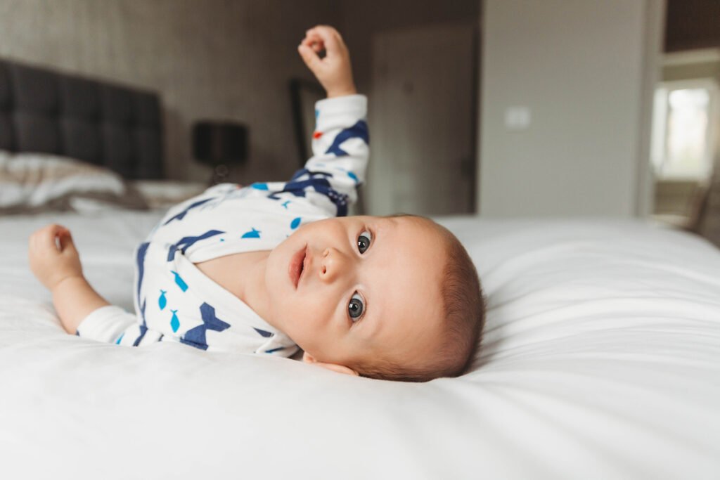 Baby lying in bed on his tummy looking at the camera. Soft natural window light.