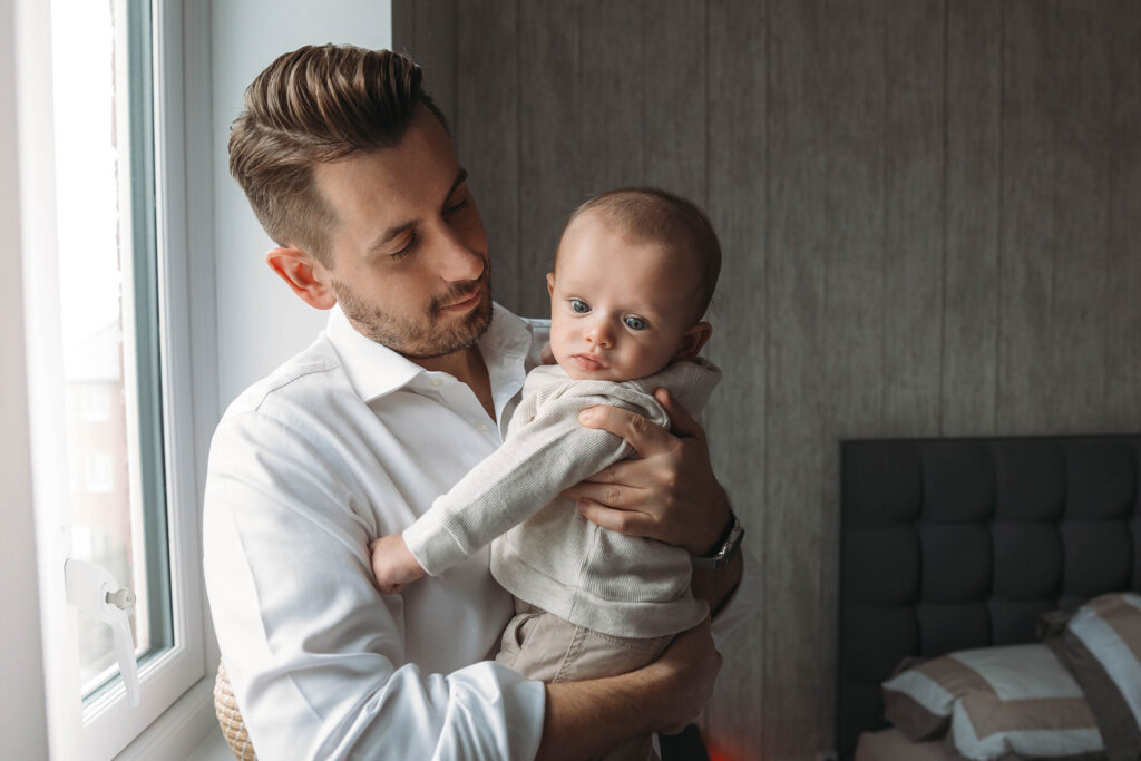 Dad holding his baby by the window.