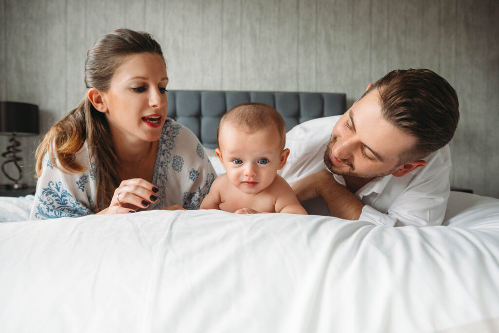 Mum and dad lying on their tummies on bed with their baby in between.