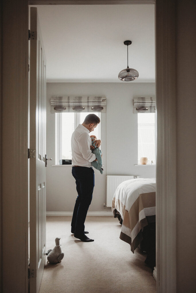 Docuentary style photo of a dad holding his baby and trying to put his to sleep.