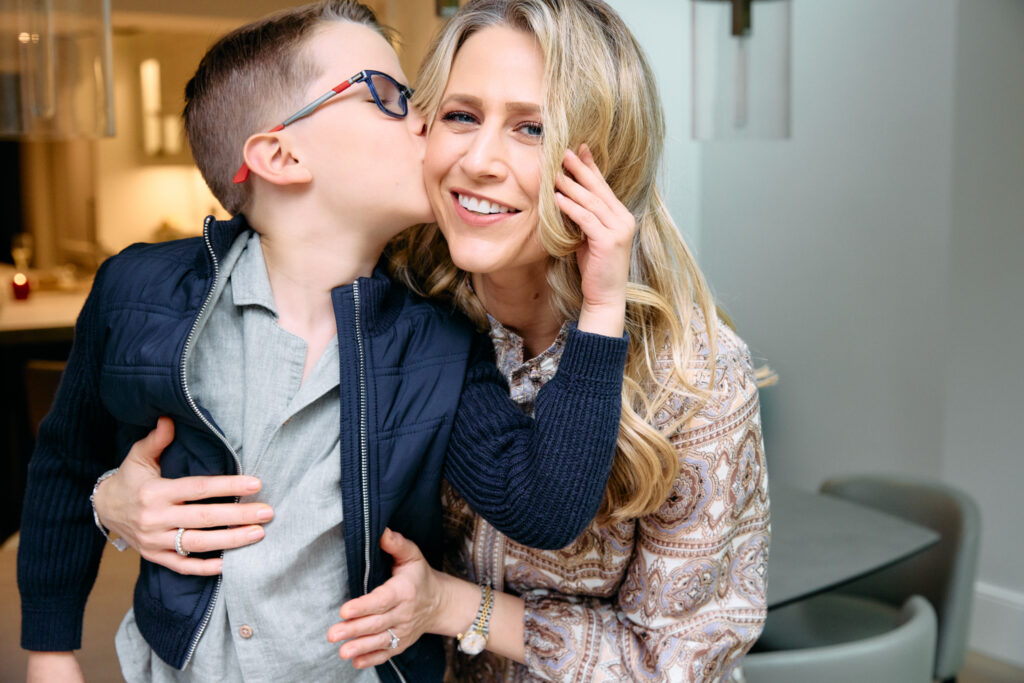 Little boy kissing his mum while mum is looking at the camera smiling.