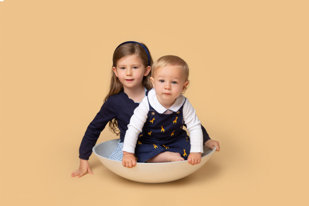 Little girl and her toddler brother posing for a photo in a bowl .