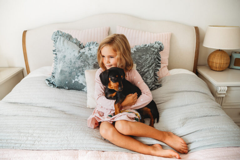 Little girl sitting on bed holding her puppy.
