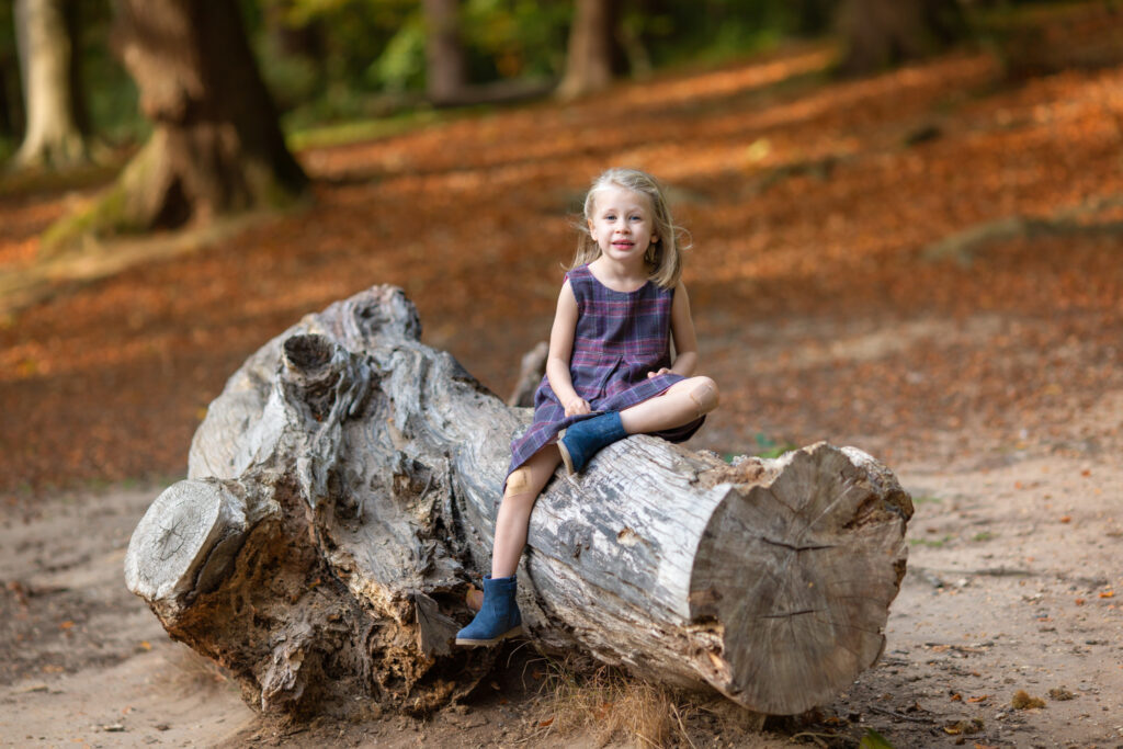 Little girl sitting on a log and smiling for a photo at the park.