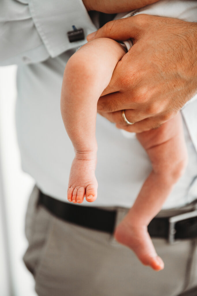 Newborn baby legs held by dad in a close up shot.