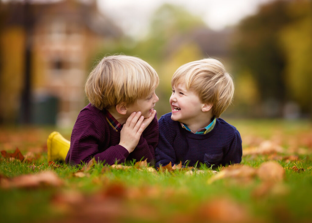 Two boys lying on the grass on their tummies looging at each other and smiling.