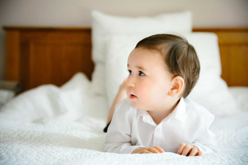 Babay lying on bed lon his tummy looking to his right.