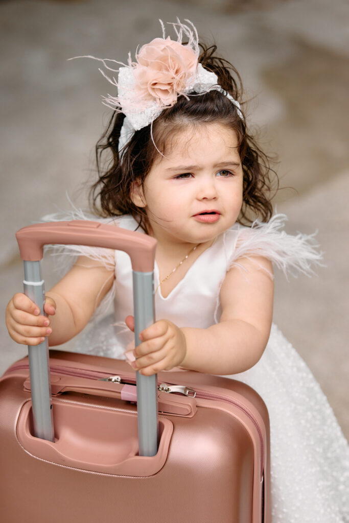 A little girl in her christening church hoding a pink suitcase.