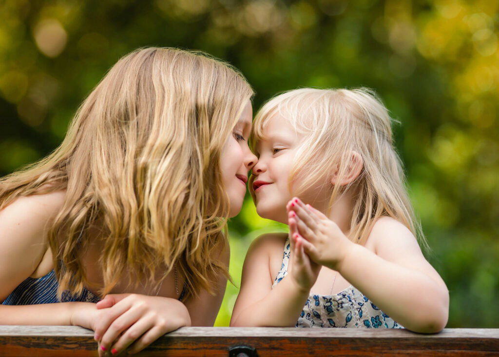 Two sisters, nose to nose looking and smiling at each other in the parl.