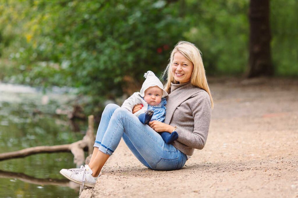 Mum holding her little boy on her lap as she is sitting by a lake at a park in London.