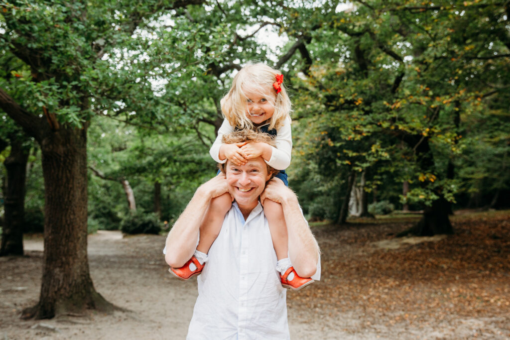 Little girl sitting on her dad's neck. Both dad and girl are smiling at the camera.