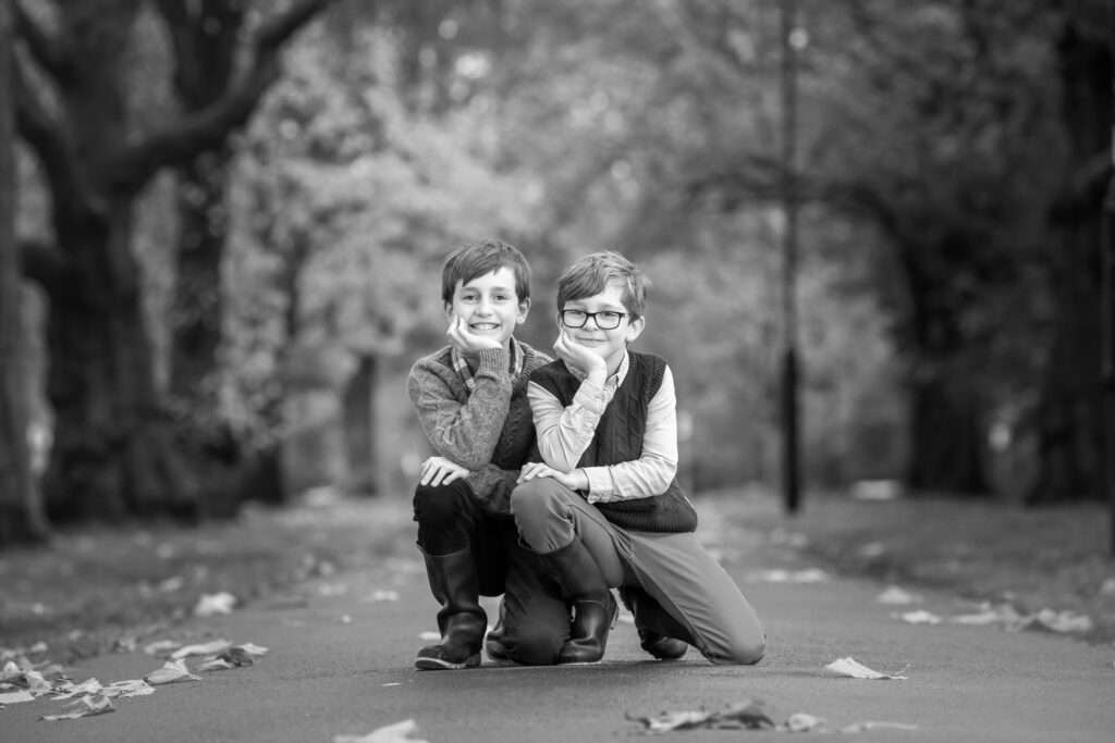 2 boys posing for a photo at the park. They are both sitting on their knees holding theri heads.