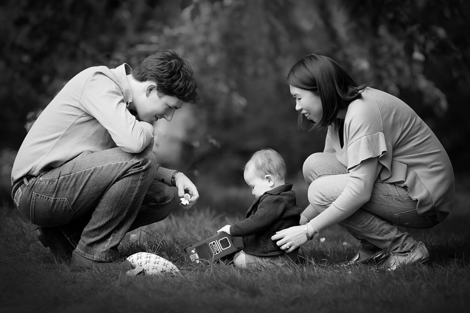 mum and dad playing with their baby boy on the grass at the park.