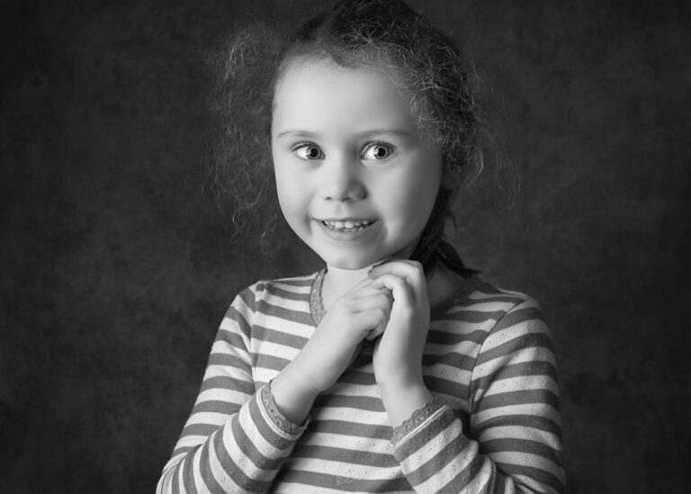 Little girl holding her hands by her chest and smiling for a portrait photo.