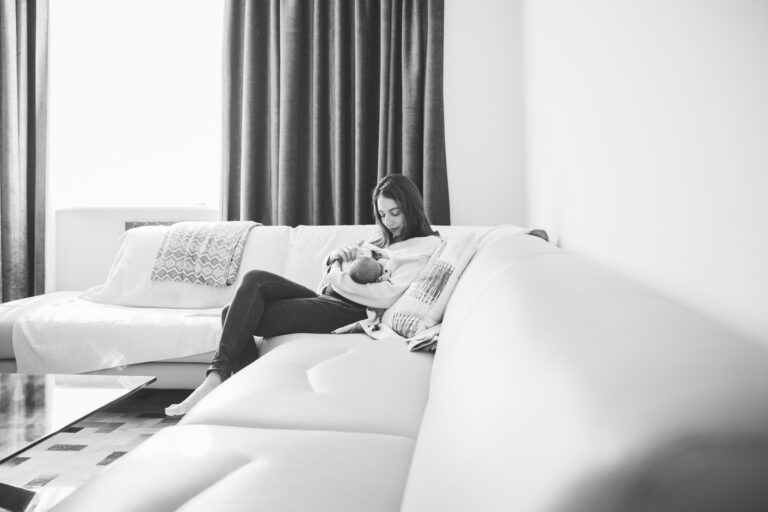 Mum sitting on a sofa holding and looking at her newborn baby.