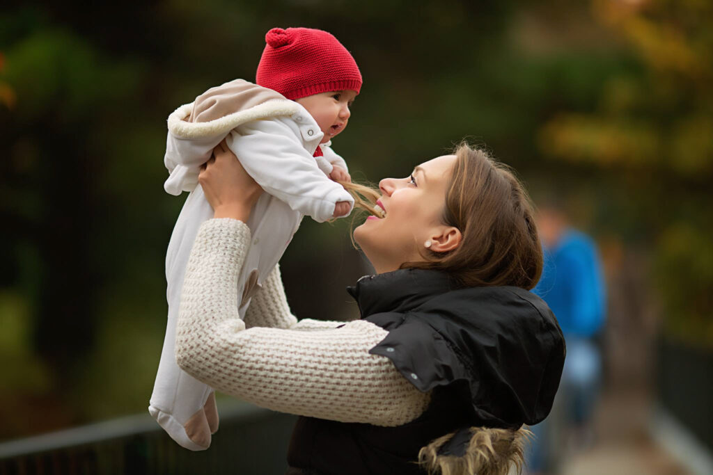 A mum holding her baby up and looking at him with love at a park in London.