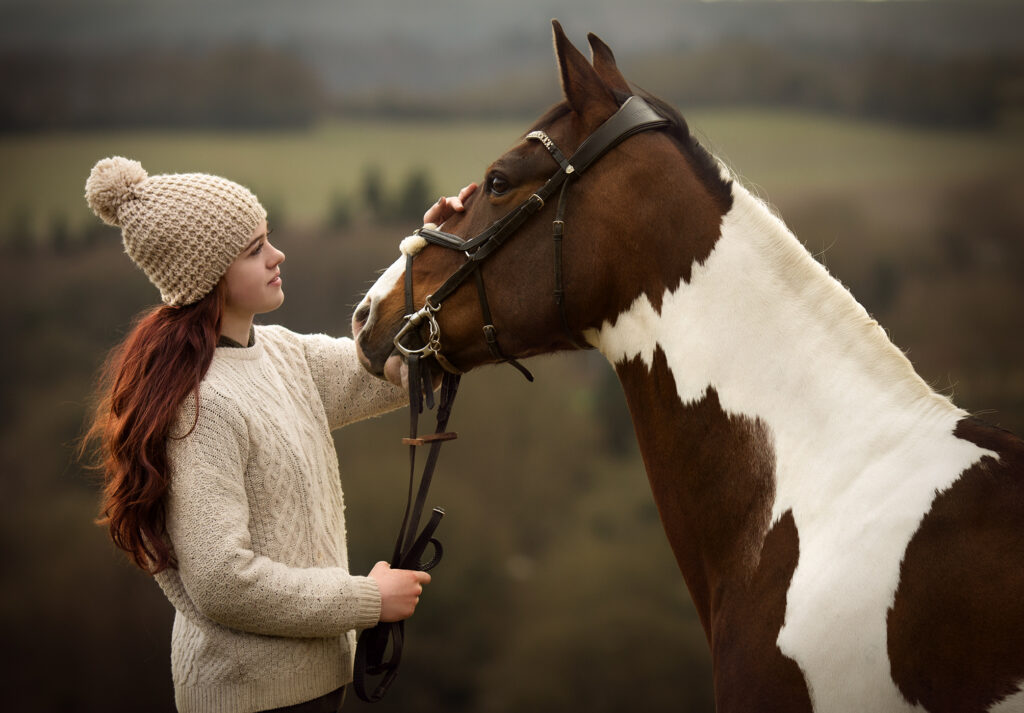 A girl touching her horse on the forhead on a cold winter day in a field in Surrey.