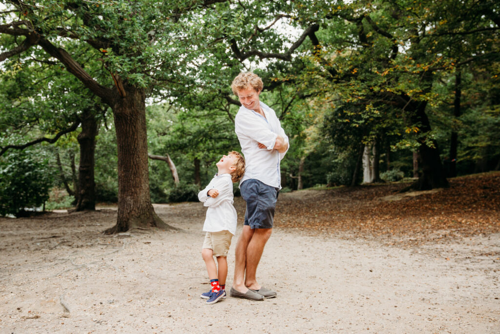 Dad and his little boy standing back to back looking at each other at Wimbledon park.