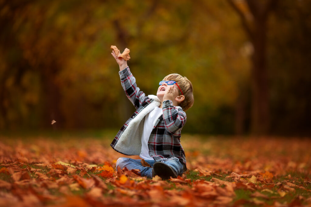 Little boy sitting down on a autumn leaves looking at the sky.