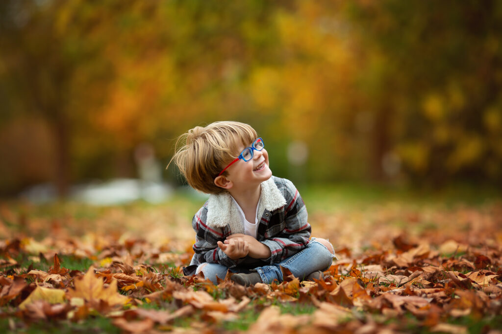 Little boy sitting on autumn leaves looking at something.