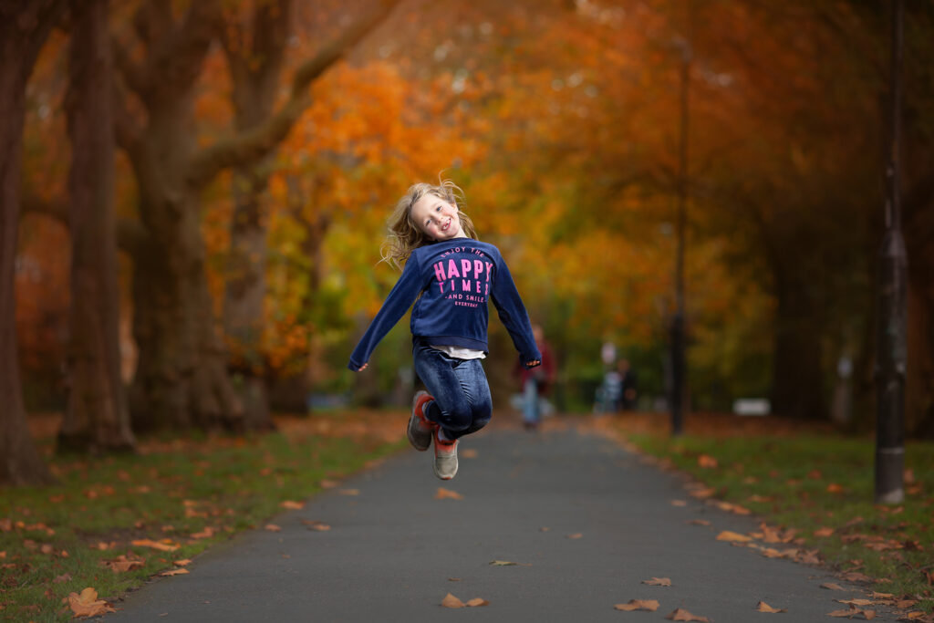 Girl jumping in a park with autumn leaves.