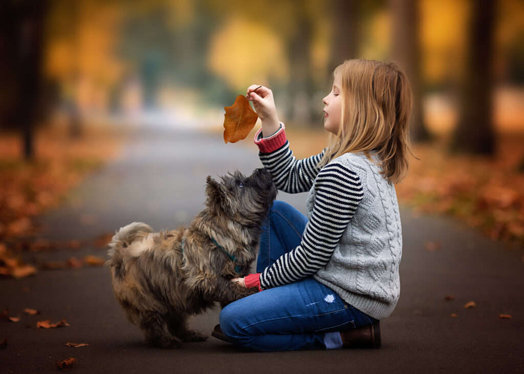 A little girl playing with her dog surrounded by autumn leaves.