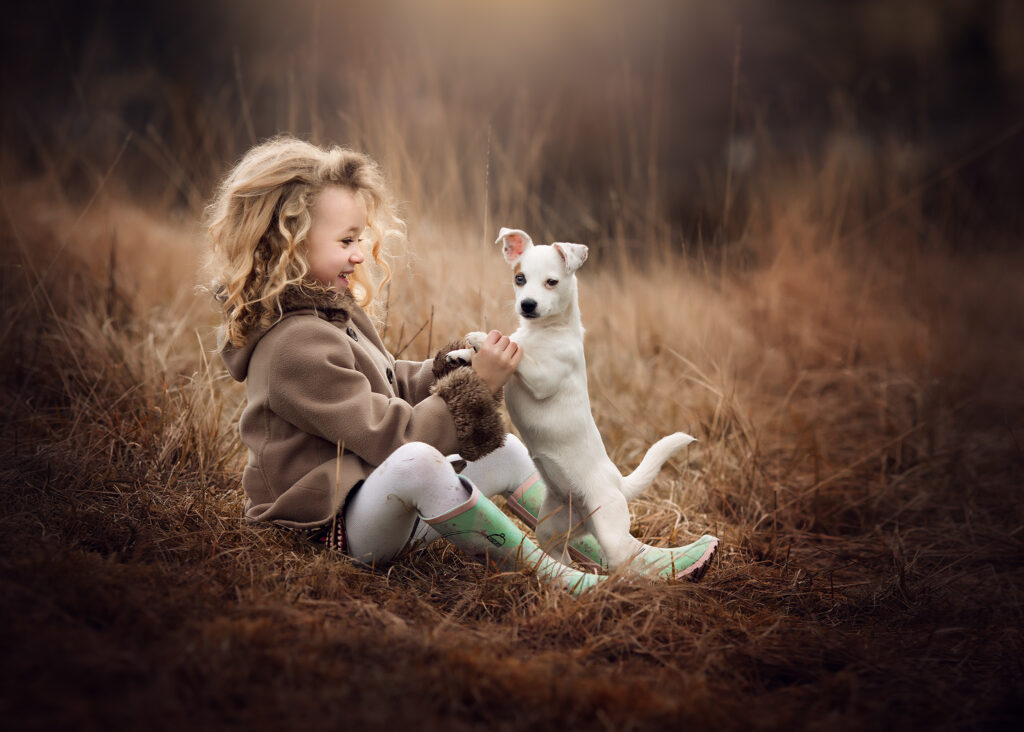 A little girl sitting down playing with her puppy in a cold winter day.