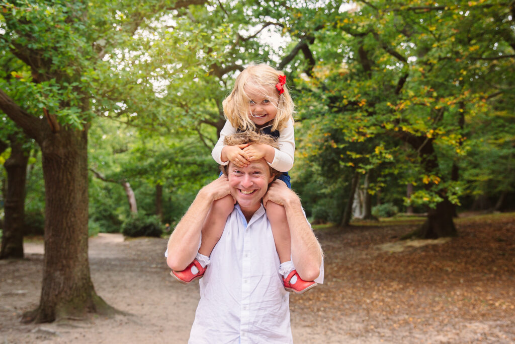 A little girl on his dad's neck in a park in Wimbledon.