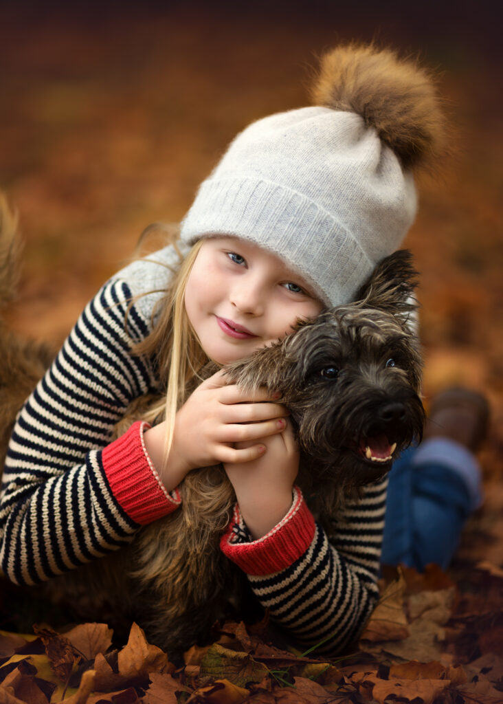 Little girl lying on the ground on autumn leaves holding her little dog.