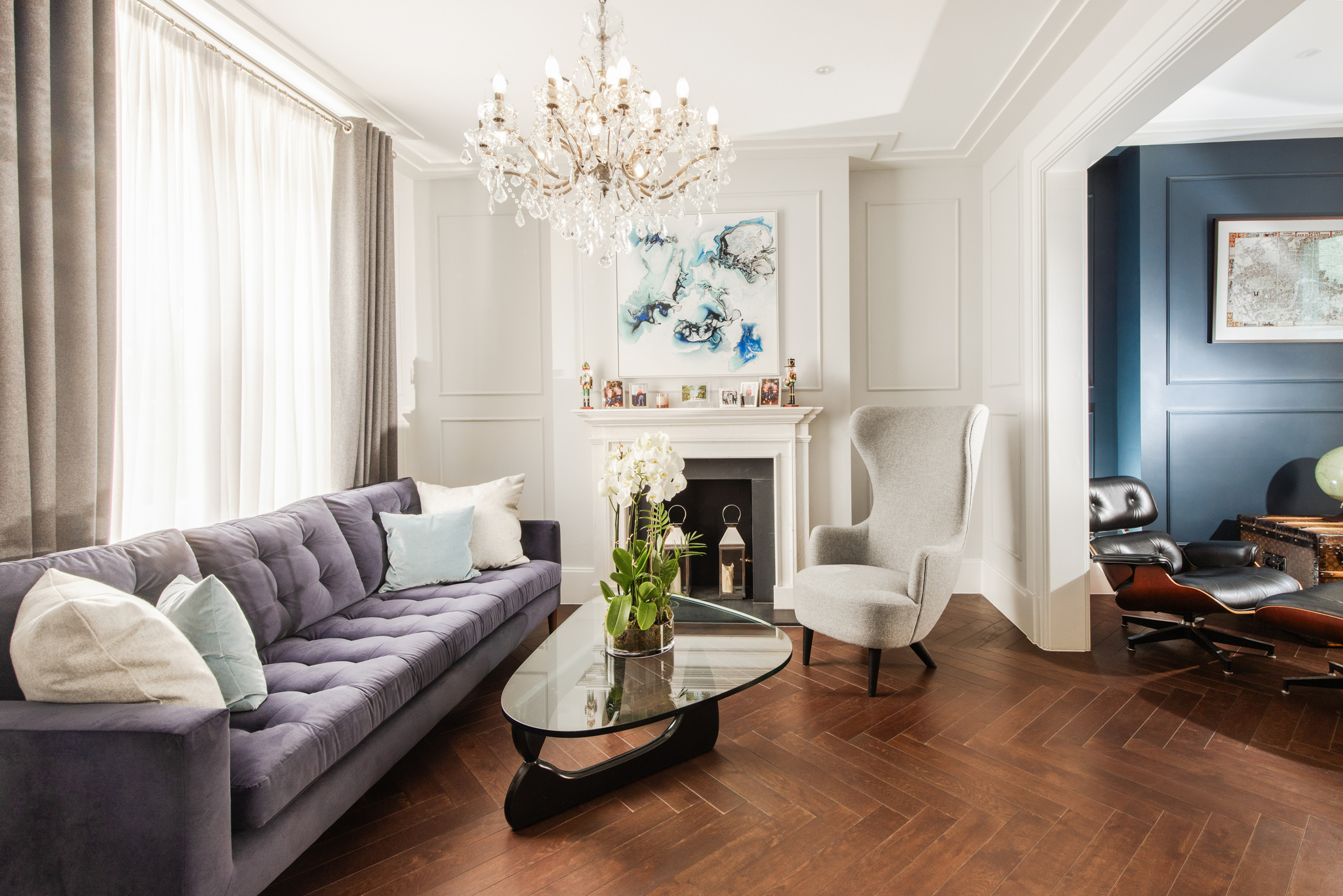 Elegant living room with purple velvet sofa, crystal chandelier, period fireplace, wooden flooring.