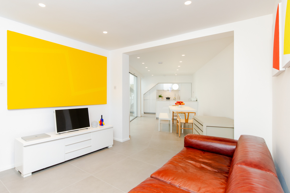 a colourful lounge showcasing a yellow wall and a kitchen further away in Pimlico London